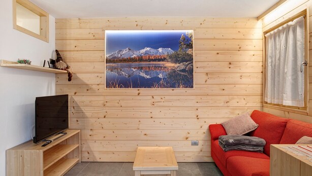Una habitación con paneles de madera, un televisor, un sofá rojo, una mesita y un cuadro con un paisaje de montañas.