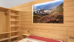 Una habitación de madera con una cama, un armario de madera y un cuadro en la pared con un paisaje de montaña.