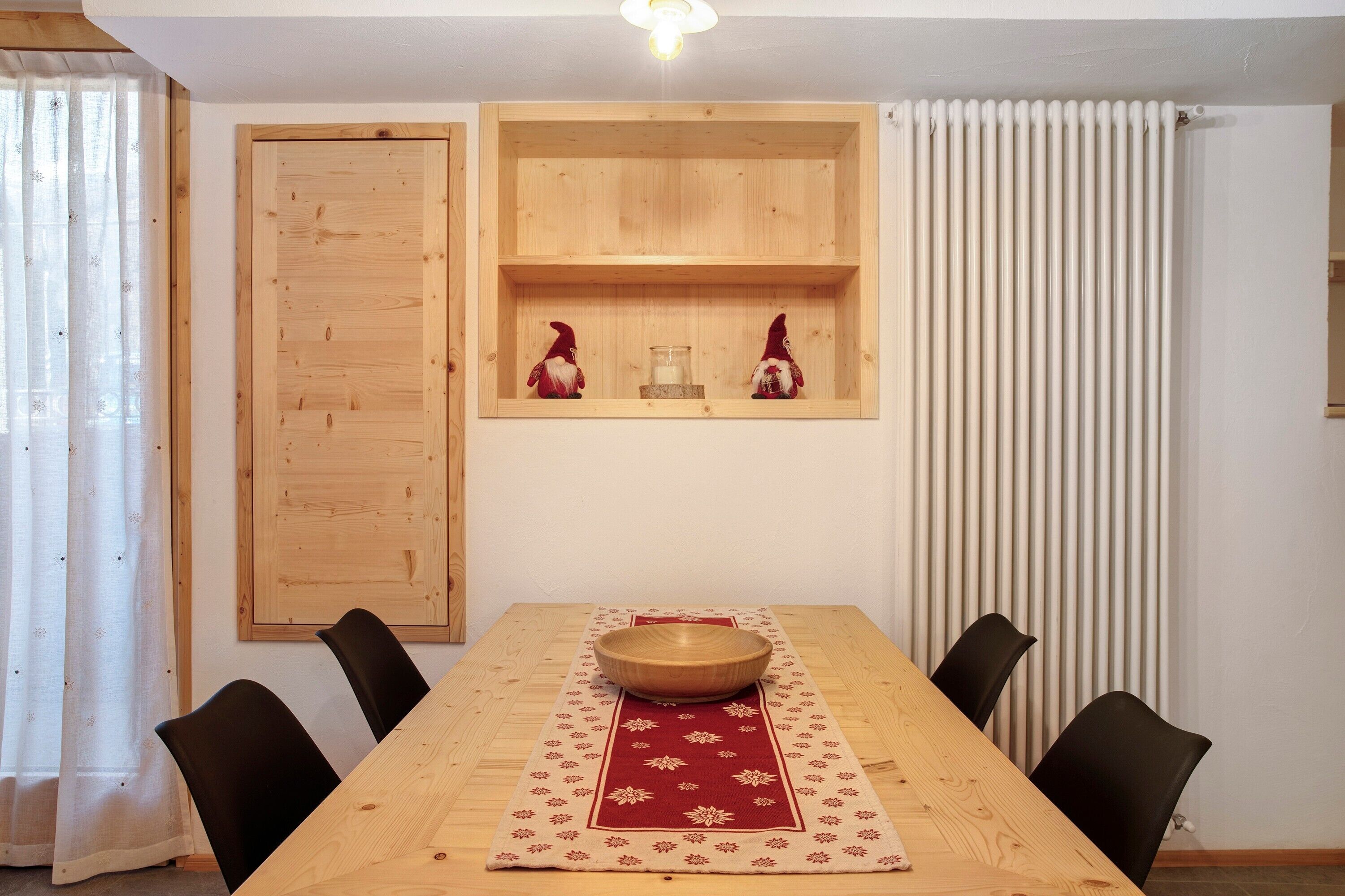 Een eethoek met een houten tafel, zwarte stoelen, een rood-wit geruit tafelkleed en twee houten planken met beeldjes.