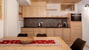 Una cocina con armarios de madera, encimera de mármol y una mesa de comedor con mantel rojo.