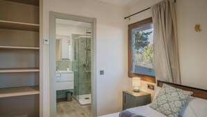 Ein Schlafzimmer mit Bett, Nachttisch, einem Fenster mit Vorhängen, einer Duschkabine und einem Schrank.