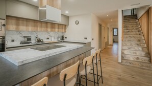 Eine moderne Küche mit Marmorarbeitsplatte, Holzschränken und einer zentralen Kochinsel mit Barhocker.