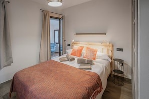 A bedroom with a bed, a bedside table, a hanging light fixture, and a view of a balcony.