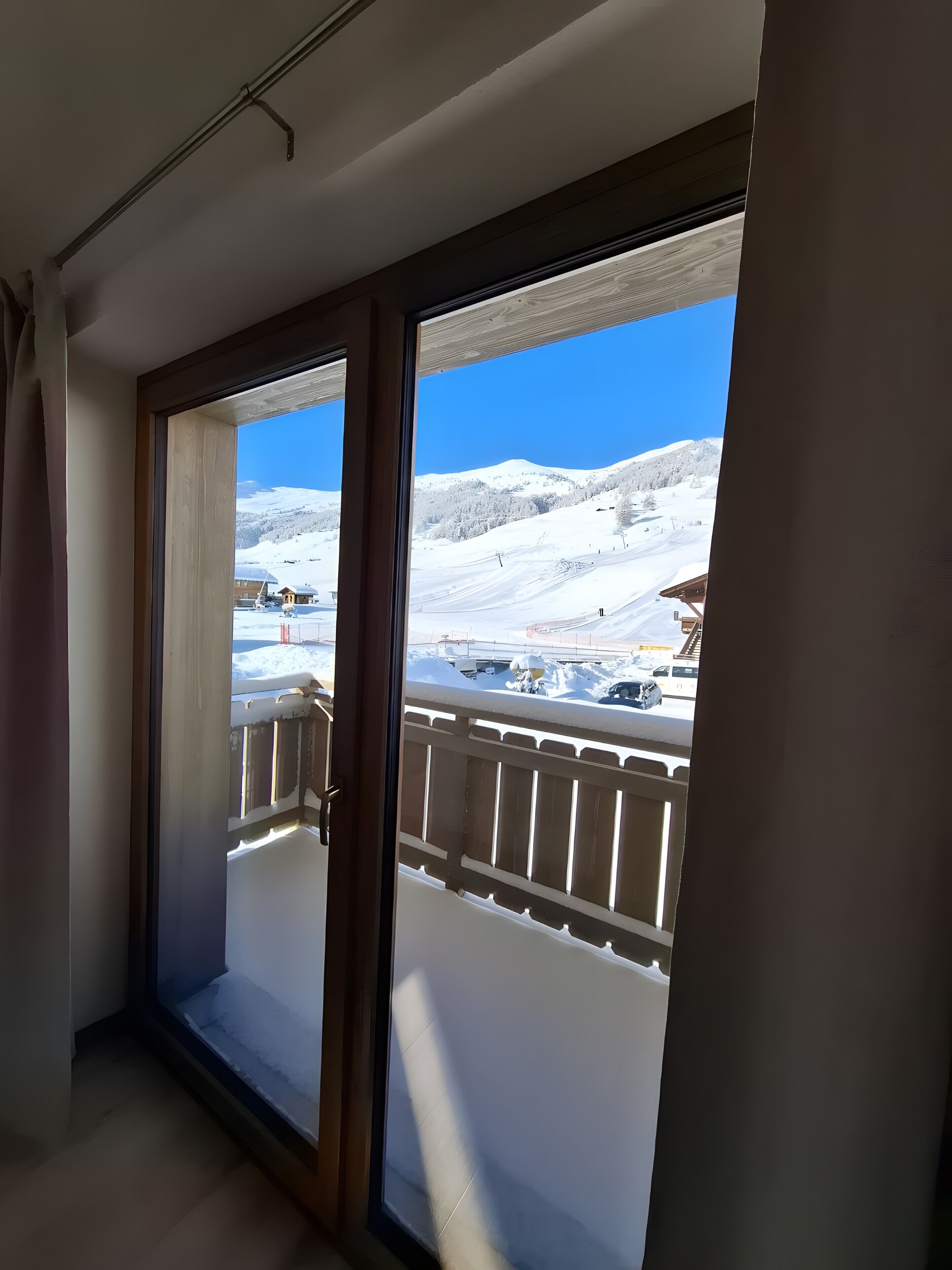 A room with a large sliding glass door leading to a balcony with a view of a snowy mountain landscape.
