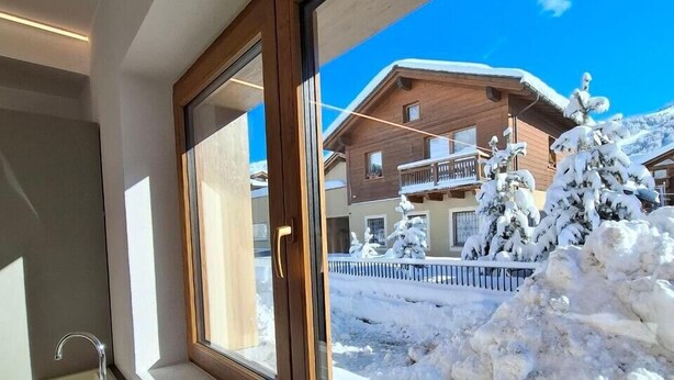A window with a view of a snow-covered landscape and a wooden building. - Studio 'Pino Mugo' with Mountain View, Balcony and Wi-Fi (Livigno)