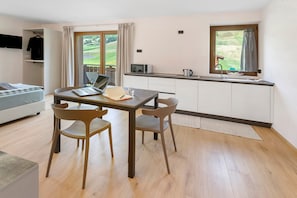 A modern room with a bed, a desk with a laptop, a small kitchen area, and a view of a green landscape. - Studio 'Pino Mugo' with Mountain View, Balcony and Wi-Fi (Livigno)