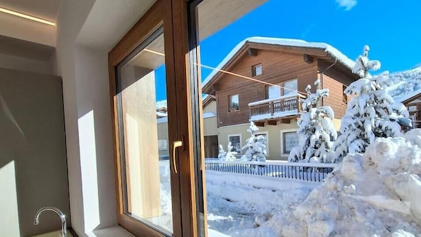 A window with a view of a snow-covered landscape and a wooden building. - Apartment 'Larice' with Mountain View, Private Garden and Wi-Fi (Livigno)