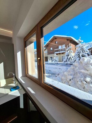 Ein Fenster mit Blick auf eine verschneite Landschaft und ein Holzbau.