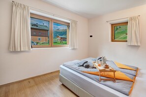 Ein Schlafzimmer mit einem Bett, einem Fenster und Blick auf ein Haus und Berge.