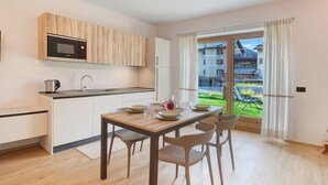 A modern kitchen with a microwave, sink, and dining area with chairs and a table. - Apartment 'Larice' with Mountain View, Private Garden and Wi-Fi (Livigno)