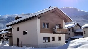 A two-story building with a balcony, surrounded by snow. - Apartment 'Larice' with Mountain View, Private Garden and Wi-Fi (Livigno)