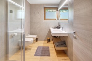 Een moderne badkamer met een glazen douchecabine, toilet, wastafel en een raam met uitzicht op een meer.