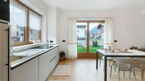 A modern kitchen with a large window, a dining area with a table and chairs, and a view of a mountain and buildings outside. - Apartment 'Stella Alpina' with Mountain View, Private Garden and Wi-Fi (Livigno)
