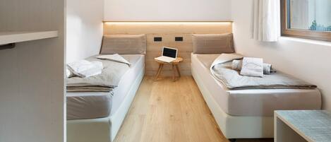 A compact room with two beds, a small table with a laptop, and a window with curtains.