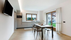 A modern kitchen with a built-in oven and microwave, a dining area with a table and chairs, and a large sliding glass door leading to a balcony. - Apartment 'Stella Alpina' with Mountain View, Private Garden and Wi-Fi (Livigno)