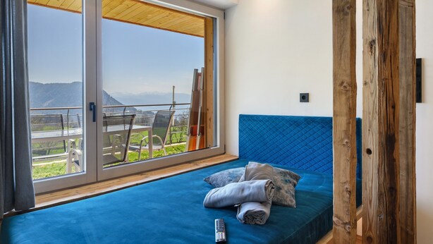 Una habitación con una cama, vista a través de un ventanal corredero y una estructura de madera.