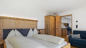 Una cama doble con cabecera de madera, un sofá azul y una kitchenette al fondo.