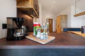 Une cuisine équipée d’une machine à café, d’une boîte de dosettes de café, ainsi que de salière et de poivrière posées sur le comptoir.