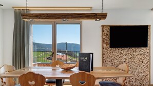 A dining area with a wooden table, heart-shaped chairs, a black book, and a TV on a stone wall.