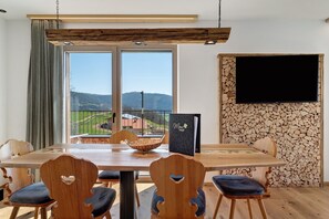 A dining area with a wooden table, heart-shaped chairs, a black book, and a TV on a stone wall.