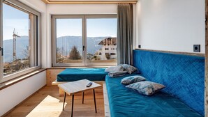 A modern room with a large window, a blue sofa, a small table, and a view of mountains.