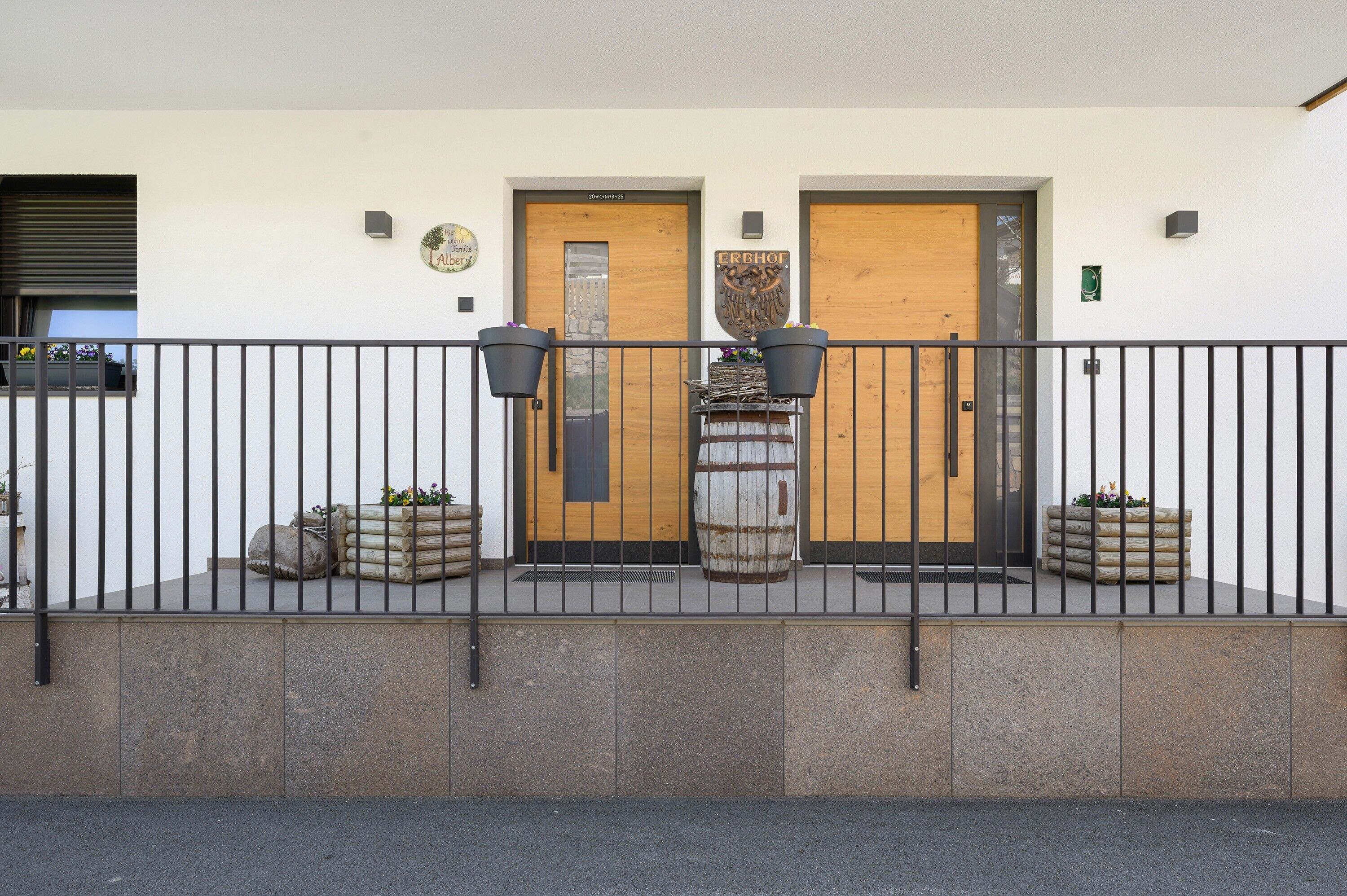 Un bâtiment doté de deux portes en bois, d’une clôture en métal et de jardinières fleuries.