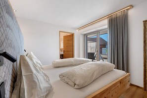 Une chambre à coucher moderne, avec un lit, une tête de lit en bois, une fenêtre avec des rideaux et une vue sur l’extérieur.