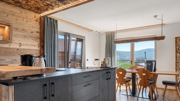 A modern kitchen with a wooden island, a dining area with wooden chairs, and a view of the outdoors.