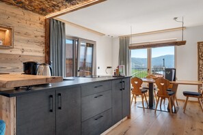 Une cuisine moderne dotée d’un îlot central en bois, d’un coin repas avec des chaises en bois et offrant une vue sur l’extérieur.