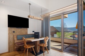 A modern dining area with a wooden table, two chairs, a flat-screen TV mounted on the wall, and a view of the outdoors through large glass doors. - Apartment 'Moarhof  Minze' with Mountain View, Shared Garden and Wi-Fi (Mölten/Schlaneid)