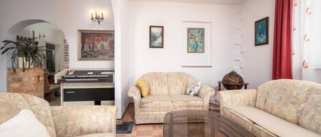 A living room with a piano, two sofas, a glass coffee table, and a brick fireplace.