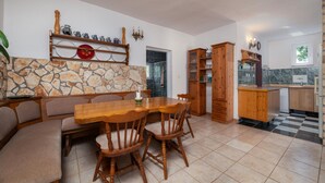 Un coin repas avec une table et des chaises en bois, un mur en pierre et une cuisine dotée de meubles en bois et d’un dosseret carrelé.