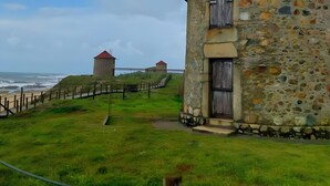 Un edificio de piedra con forma circular y techo a dos aguas, situado en una colina cubierta de hierba con vista al mar.