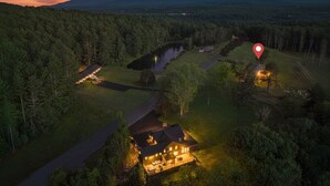 Oversigtsbillede af et hus omgivet af tæt skov, med en sø i nærheden og et bjerglandskab i baggrunden.
