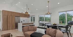 A modern kitchen with wooden cabinets, a dining area with a table and chairs, and a large window offering a view of the outdoors.
