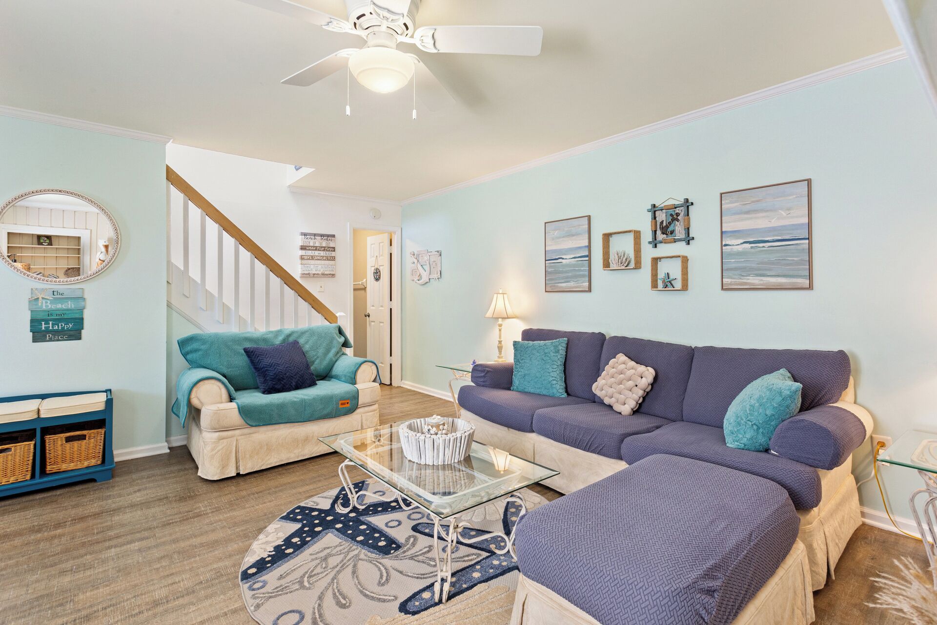 A living room with a staircase, a glass coffee table, and a blue and white patterned rug.