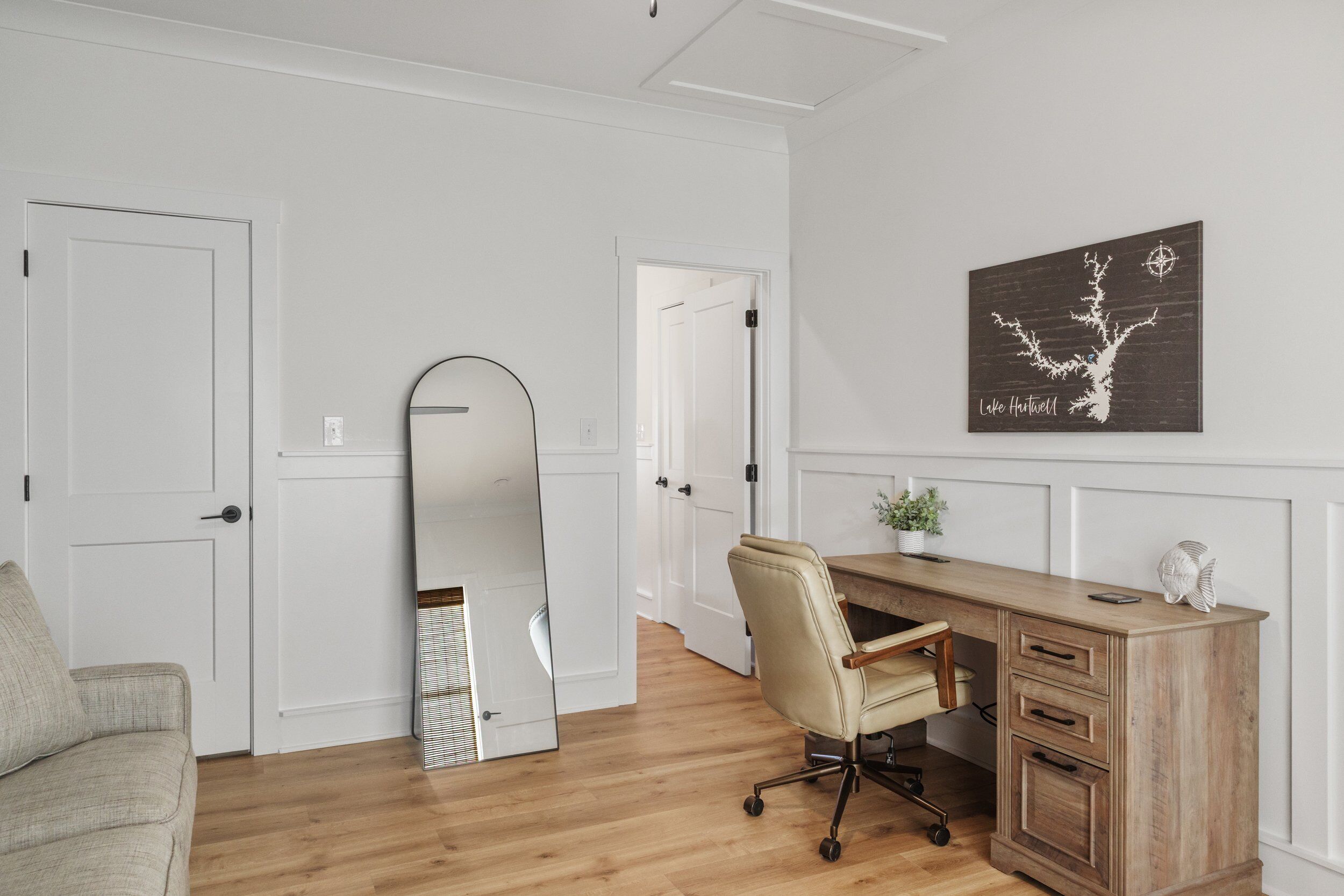 A room with a wooden desk, a chair, a mirror, and a wall-mounted artwork.