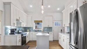 Une cuisine moderne avec des meubles blancs, un îlot central, des appareils en acier inoxydable et un plan de travail en bois.
