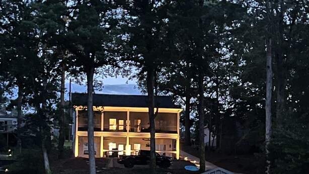 Une maison avec une jetée qui s’avance sur un lac paisible, entourée d’arbres.