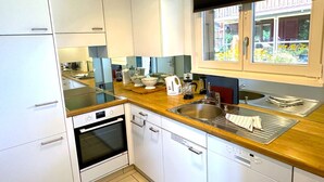 Una cocina moderna con armarios blancos, encimera de madera, horno empotrado y ventana con vista a un jardín.