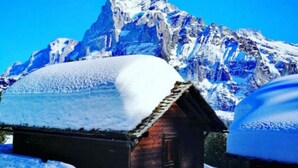 Une cabane en bois recouverte de neige, avec une montagne en arrière-plan.