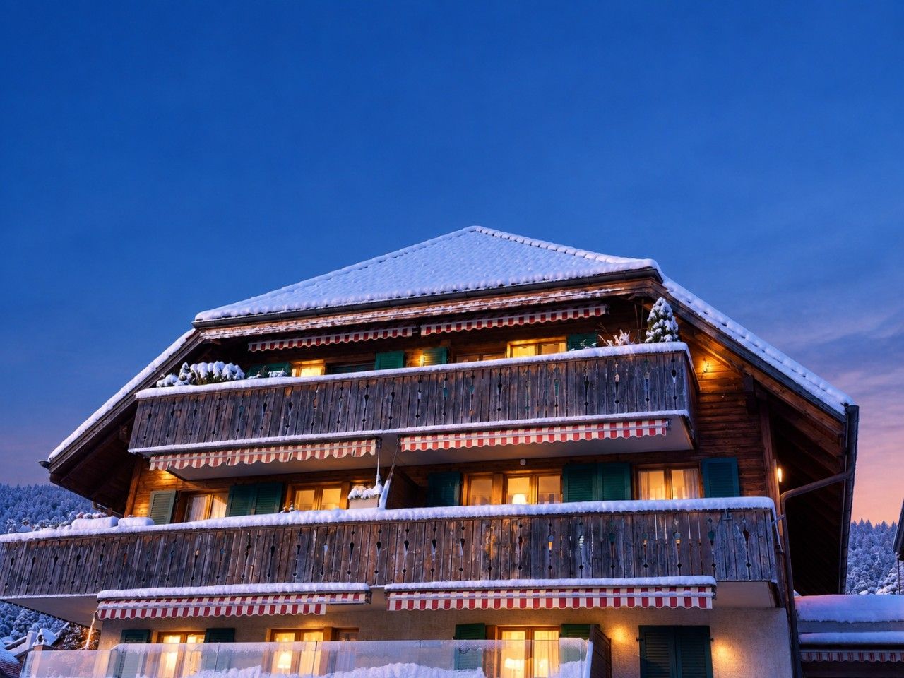 Una cabaña de madera de varios pisos con balcones, nieve en el techo e iluminación cálida en el interior.