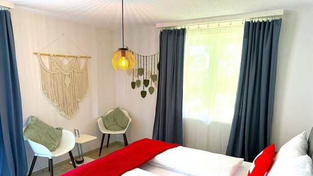 A hotel room with a bed, two chairs, a small table, and a macrame wall hanging. - Concierge, Lake Thun/Alps Scenic Views by SwissHut (Hilterfingen)