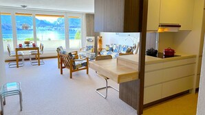 A modern kitchen with a dining area, large windows with a view of a lake, and a small island with a sink.