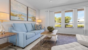 Una sala de estar moderna con un sofá azul, una mesa de centro y vistas al exterior a través de amplios ventanales.