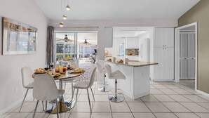 Una cocina moderna con armarios blancos, un comedor con una mesa redonda y sillas, y vistas al comedor contiguo.