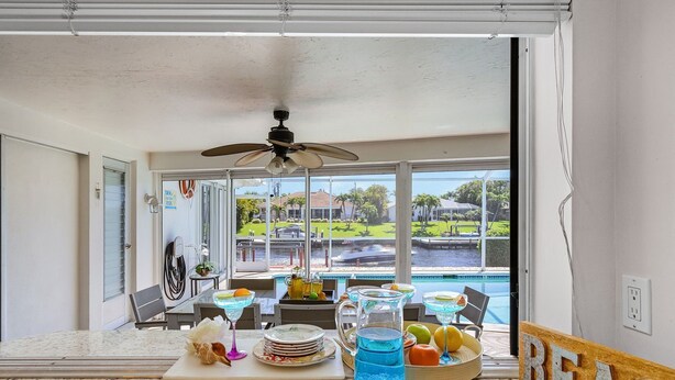 Una cocina con un amplio ventanal con vistas a una piscina, un ventilador de techo y un cartel que dice 'BEACH'.