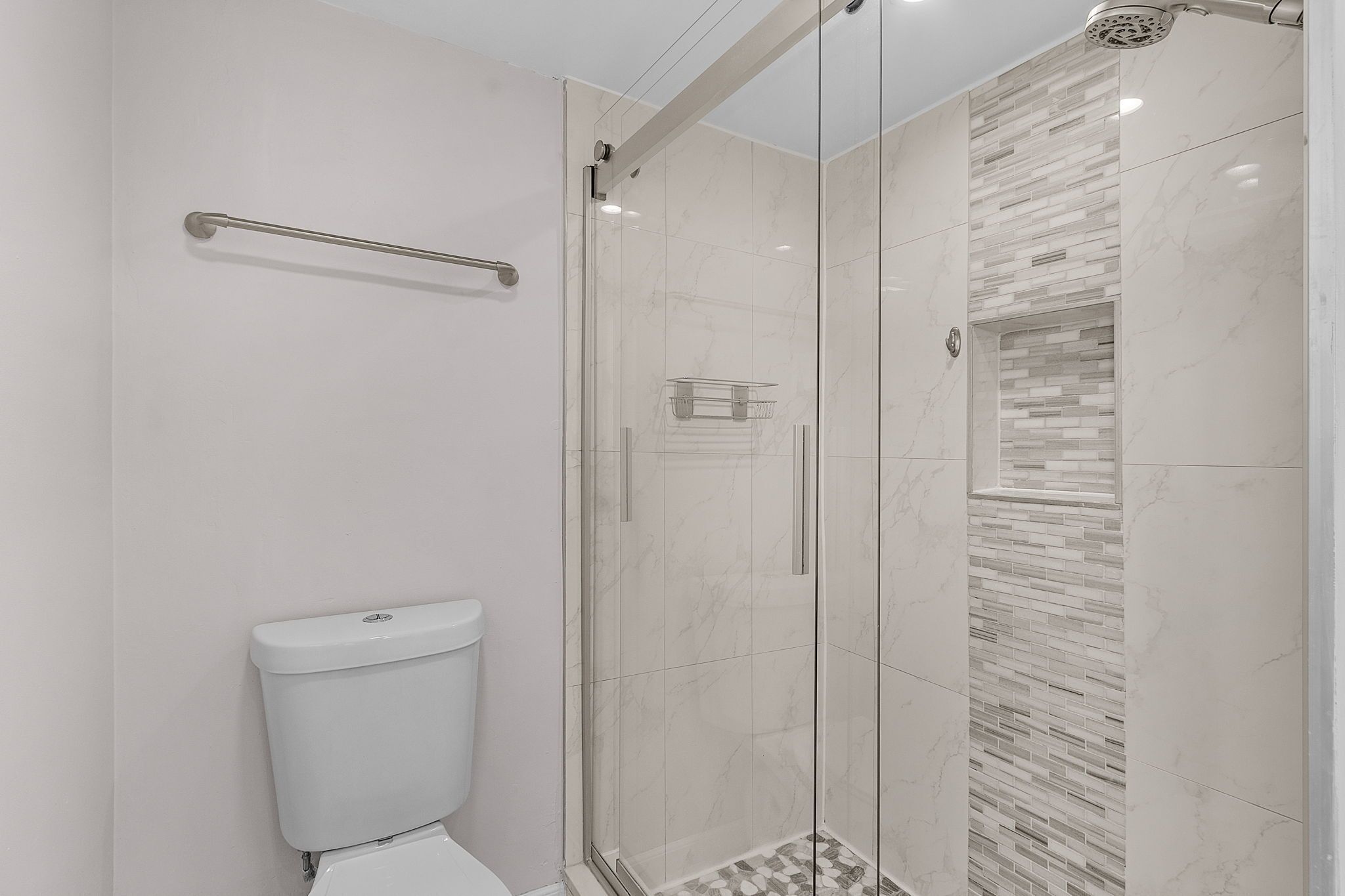 A modern bathroom with a glass-enclosed shower, a white toilet, and a tiled shower wall.
