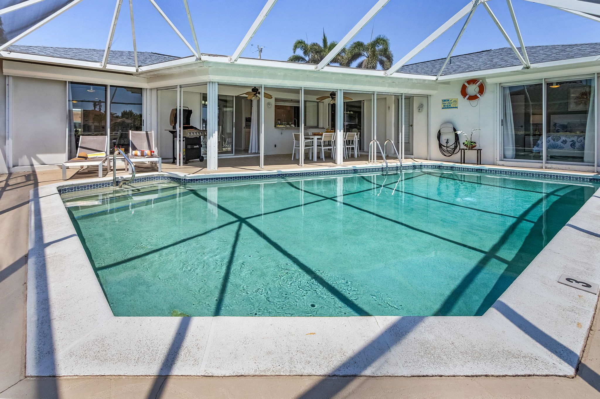 Une piscine avec un patio couvert, un barbecue et un espace repas équipé de chaises et de tables.