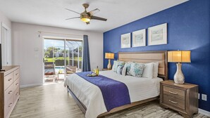 Un dormitorio con cama, mesitas de noche, ventilador de techo y vistas al exterior a través de un ventanal.